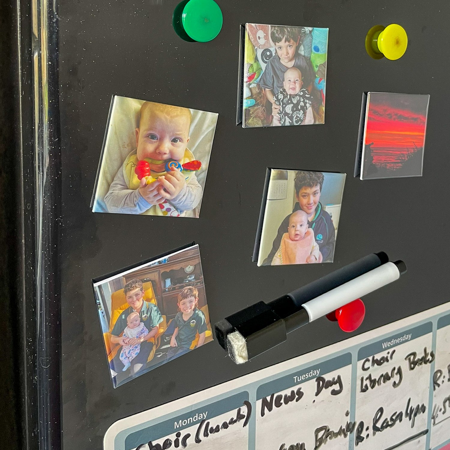 Fridge with personalised photo magnets  and a marker stuck on the black surface